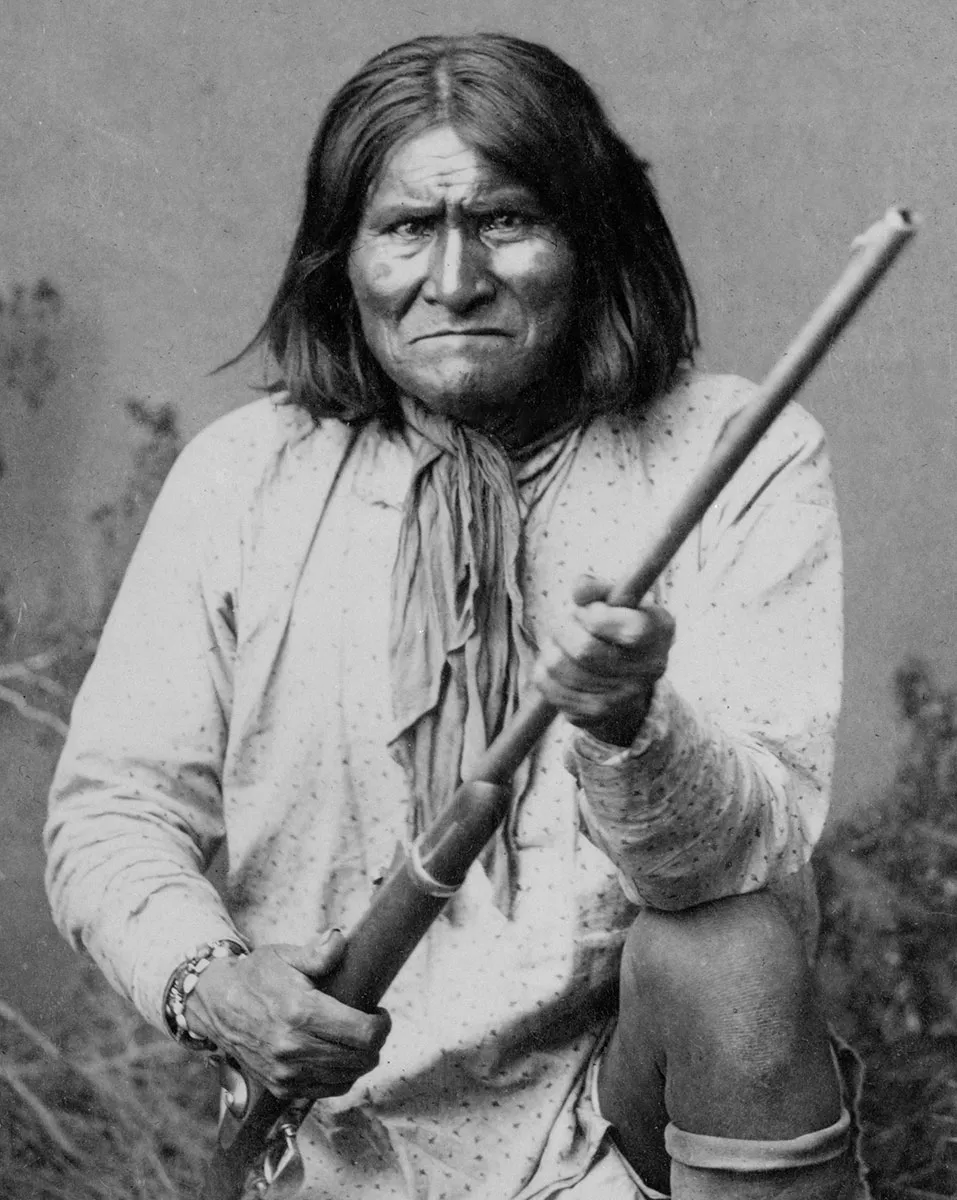 Black-and-white photograph of a Native American (Apache) man kneeling and holding a rifle
